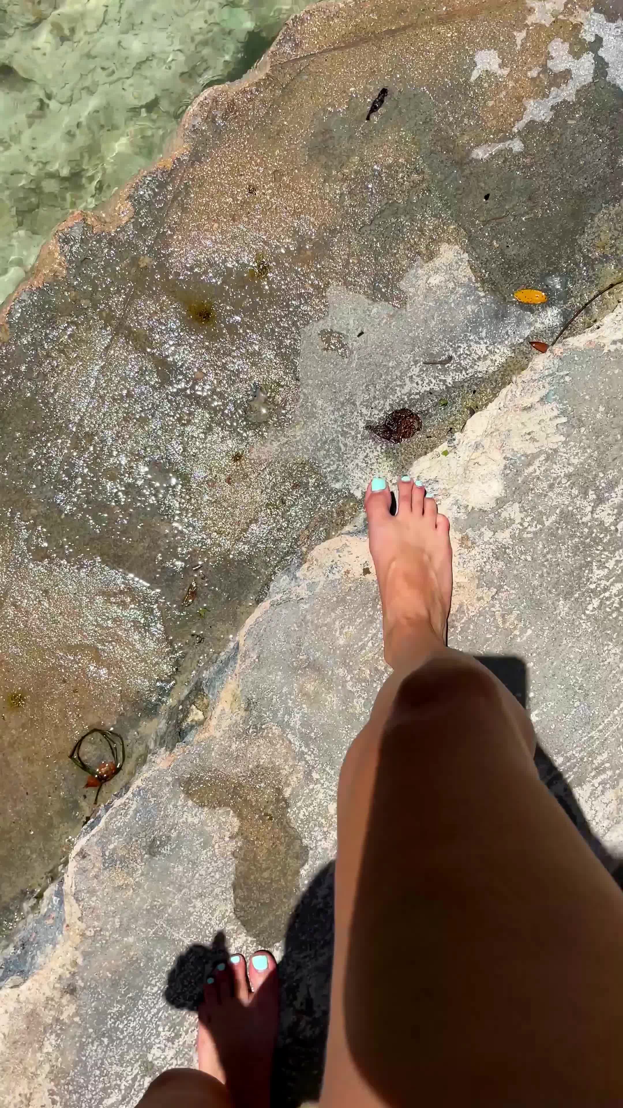 two bare feet on sunny wet rocky edge beside clear water