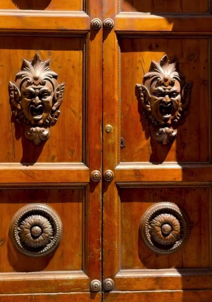 Carved lion-head door knockers on an old wooden door in Italy