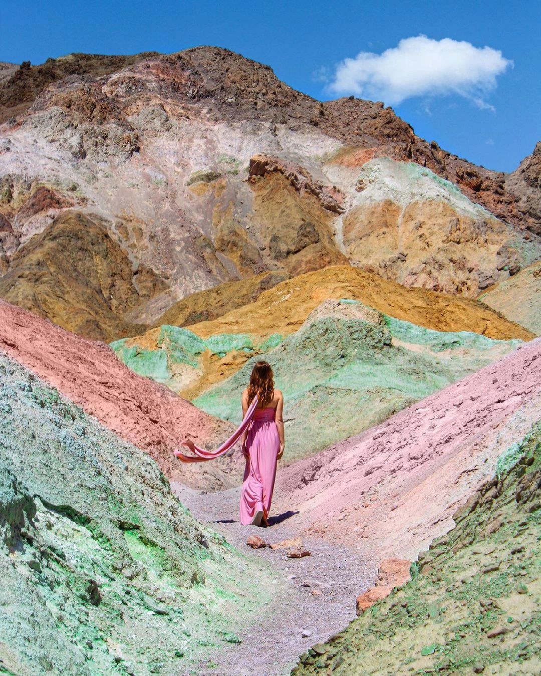 Woman in pink dress walking on colorful mountain path.