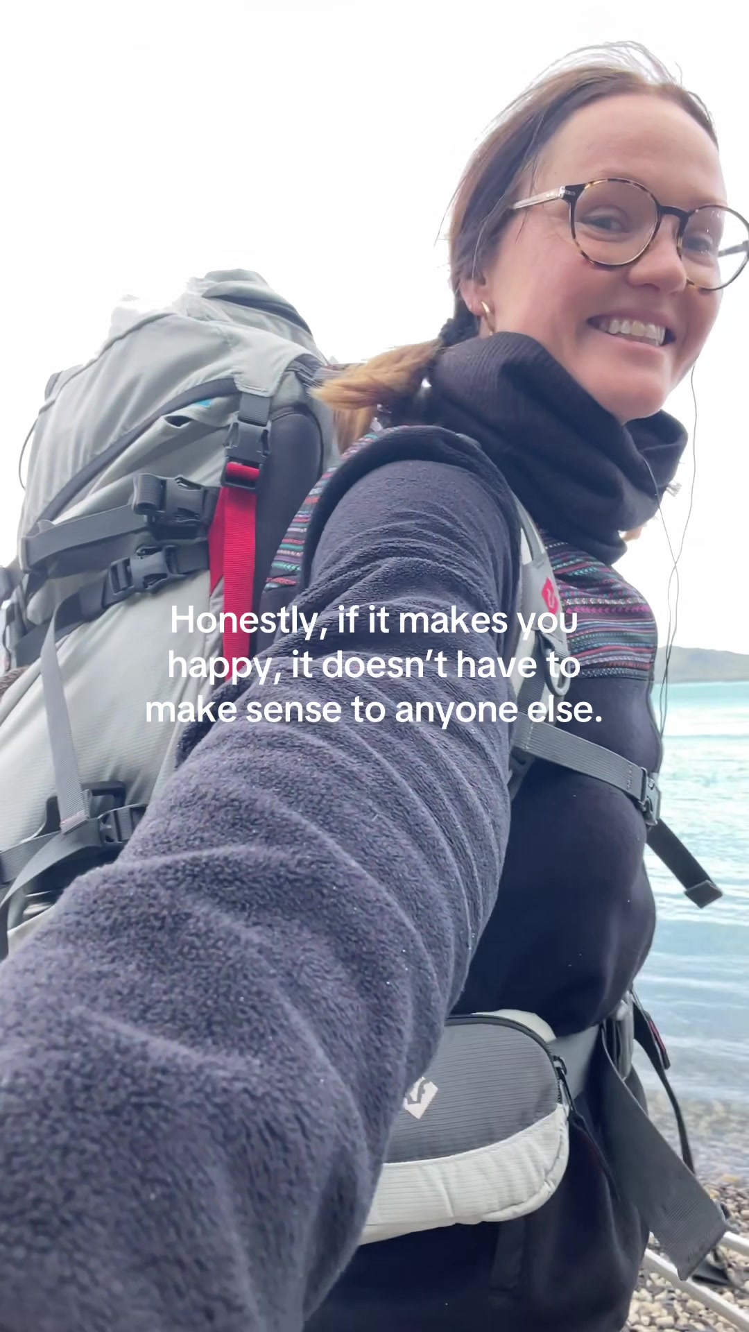 smiling woman wearing glasses and backpack by a body of water