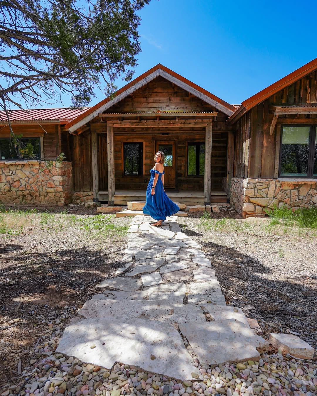 Polina in a blue dress in front of a wood and stone cabin at Zion Mountain Ranch