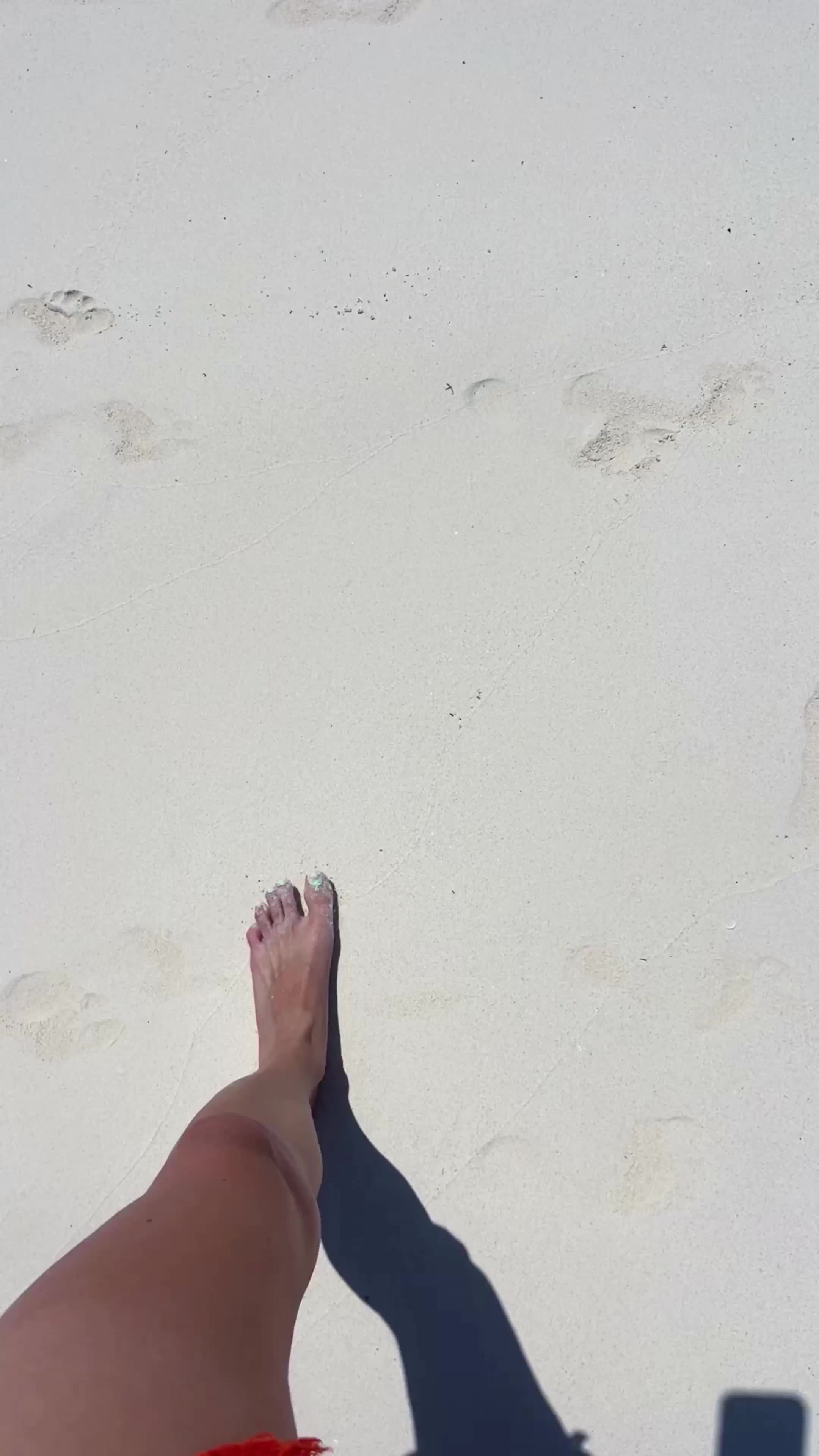a bare foot stepping on smooth white sand with several footprints around