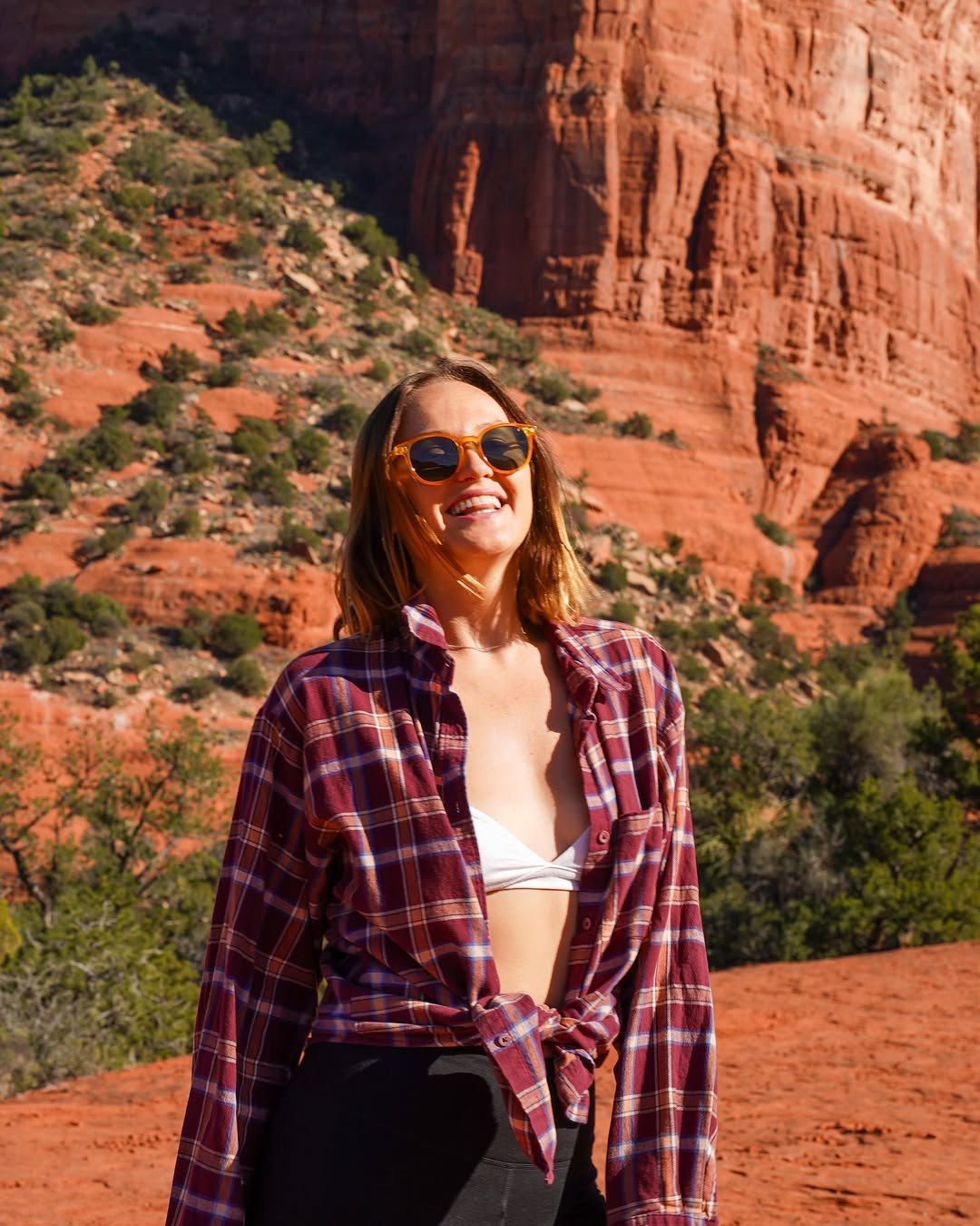 Polina smiling in a plaid shirt with the red rock of Bell Rock behind her