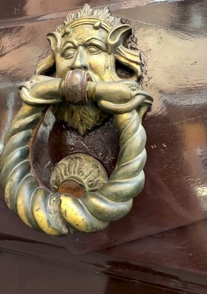 A brass door knocker shaped like a face on a door in Italy