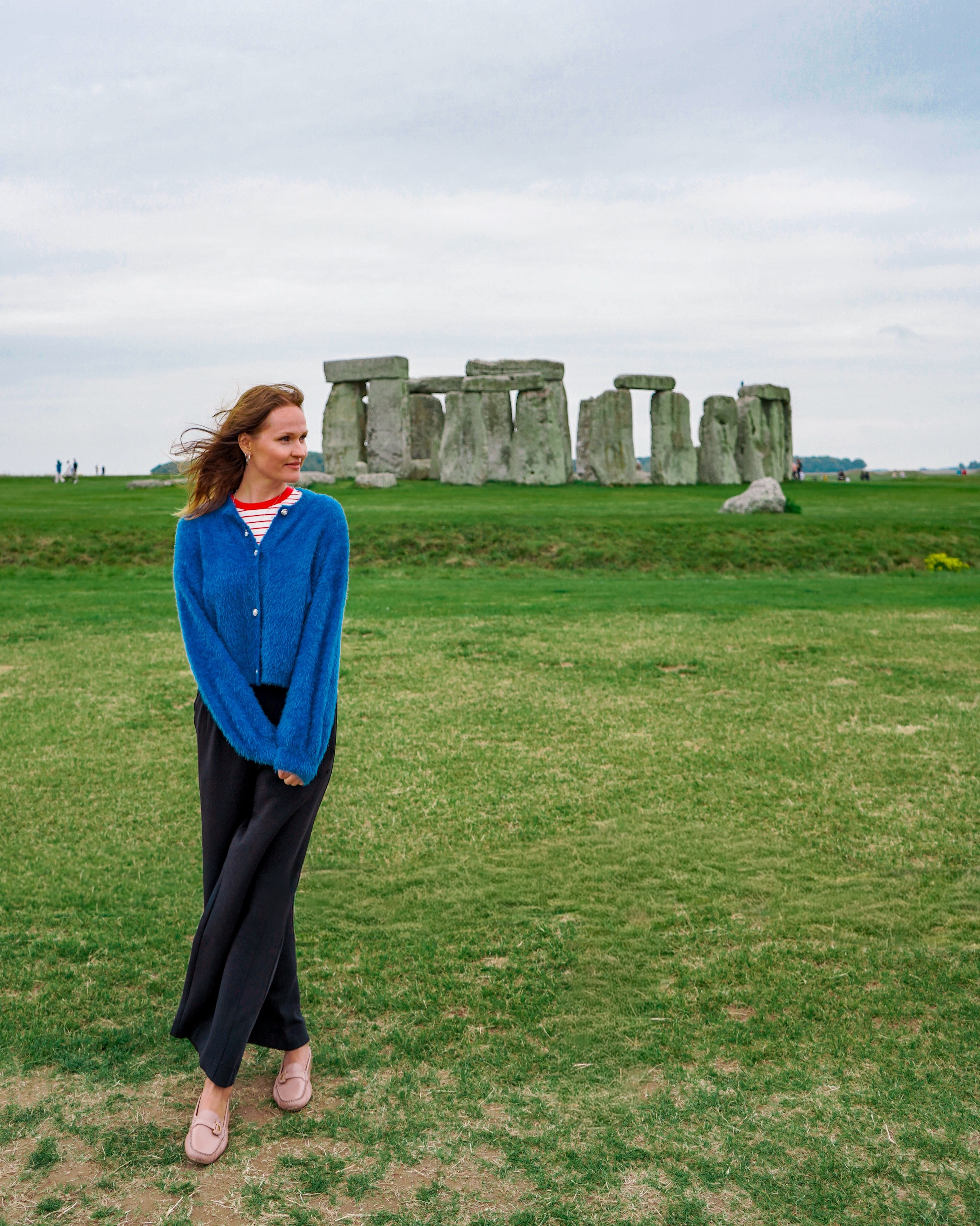 Polina standing in a green field with the stones of Stonehenge behind her