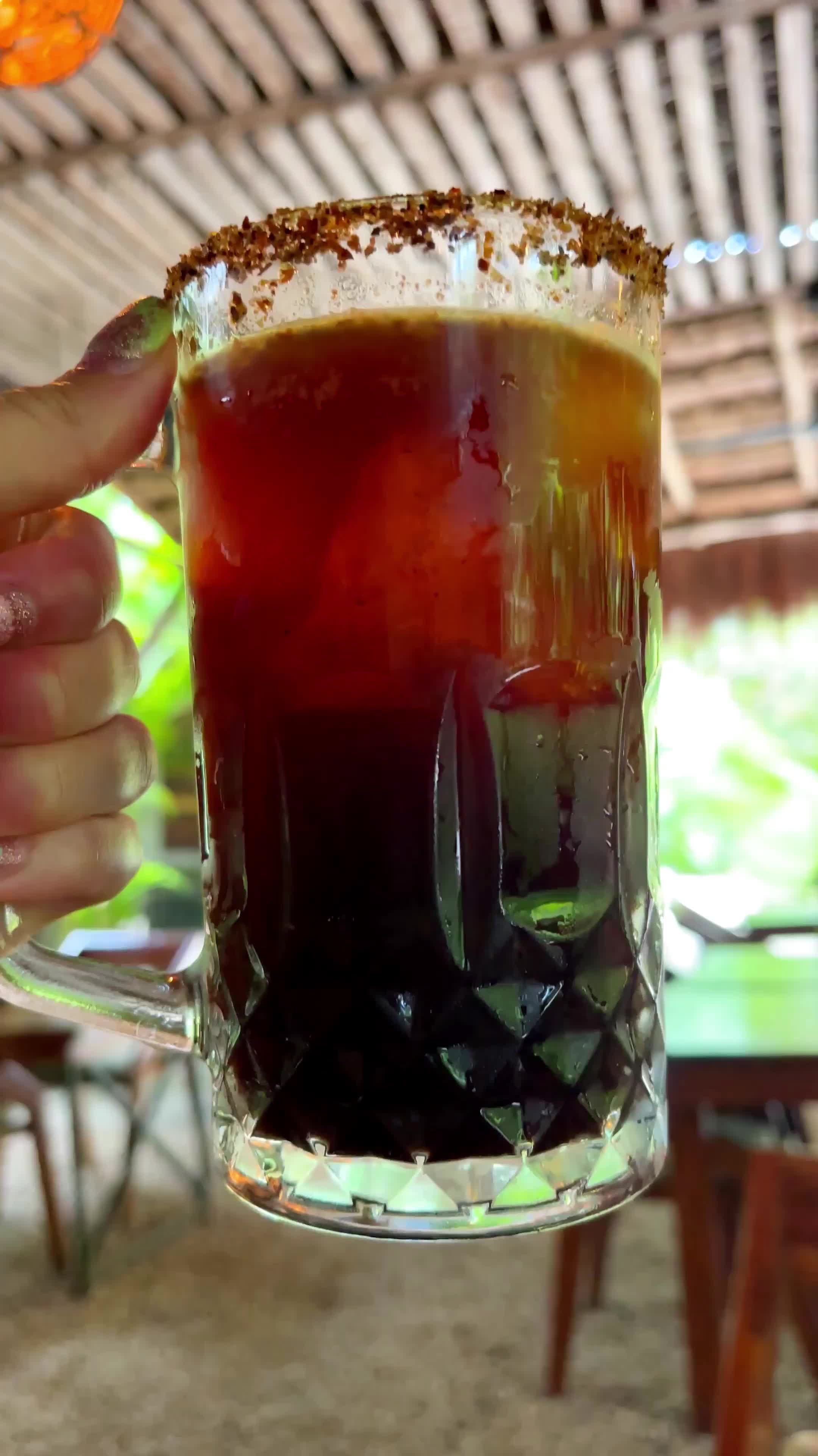 hand holding a glass mug filled with a dark beverage with a chili powder rim