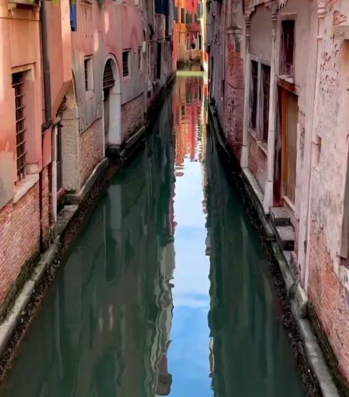 A narrow canal between pink and orange buildings in Venice