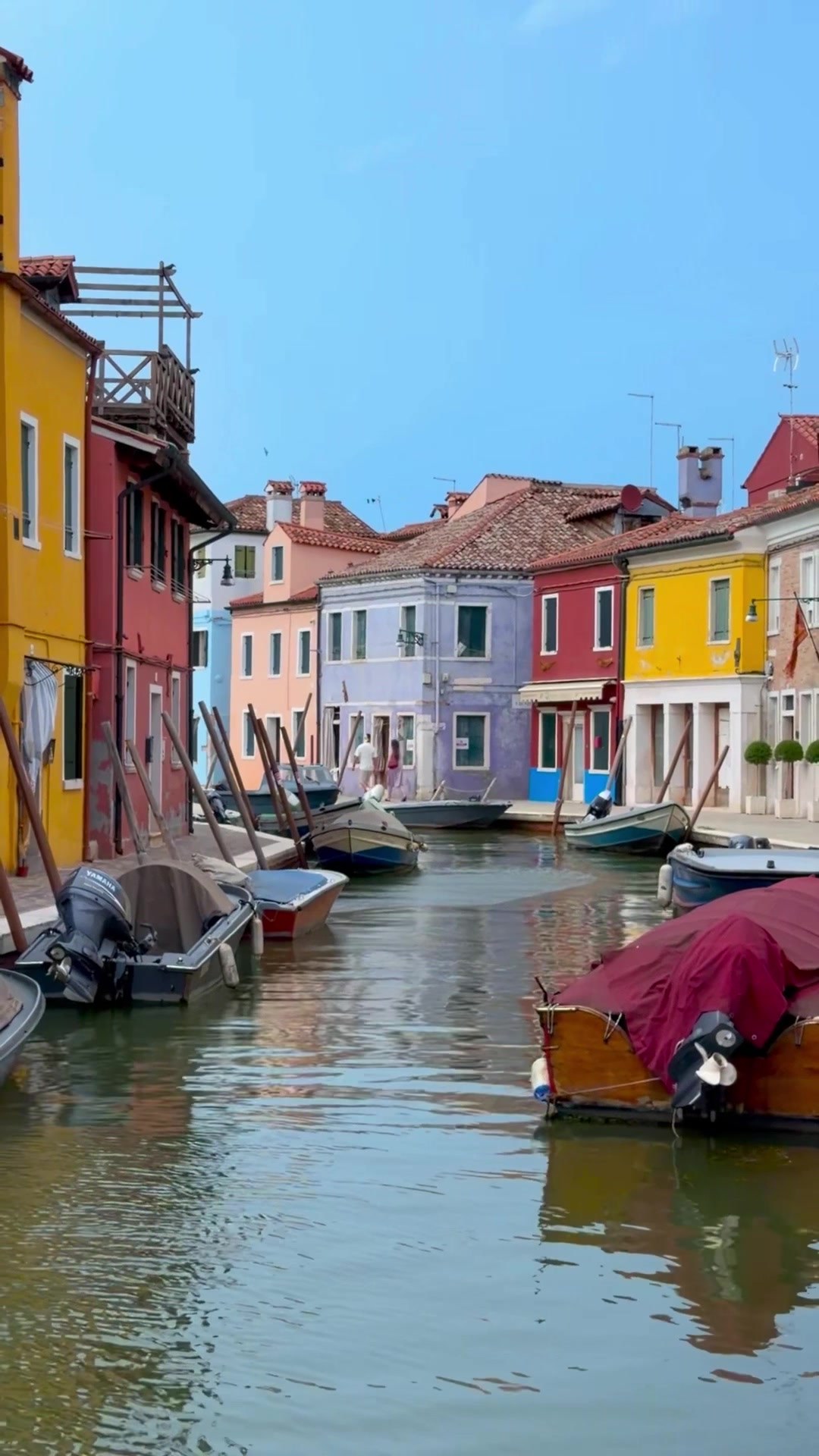 Boats moored on a canal between colorful houses on Burano