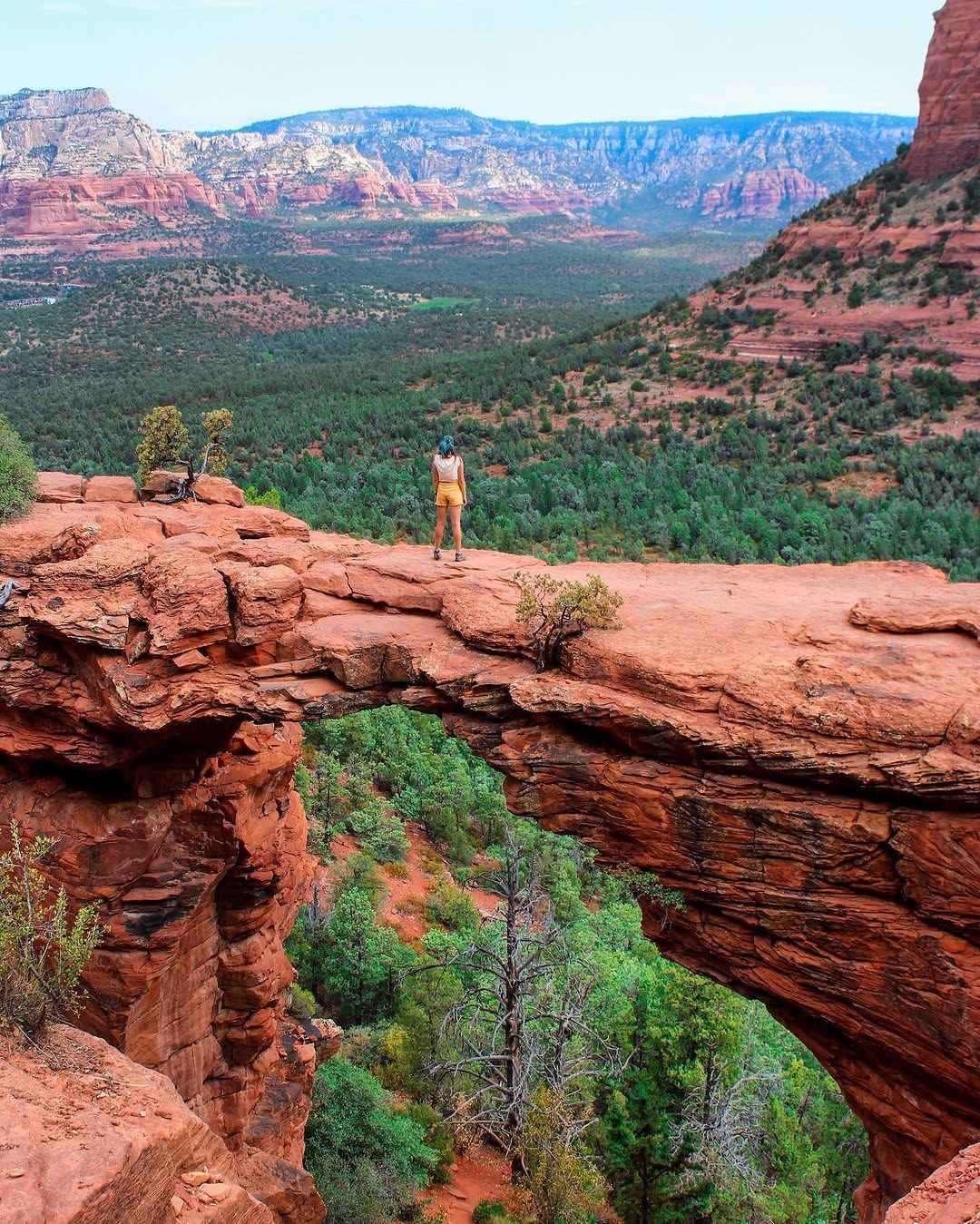 Polina standing on top of Devil's Bridge, a red sandstone arch above green desert in Sedona