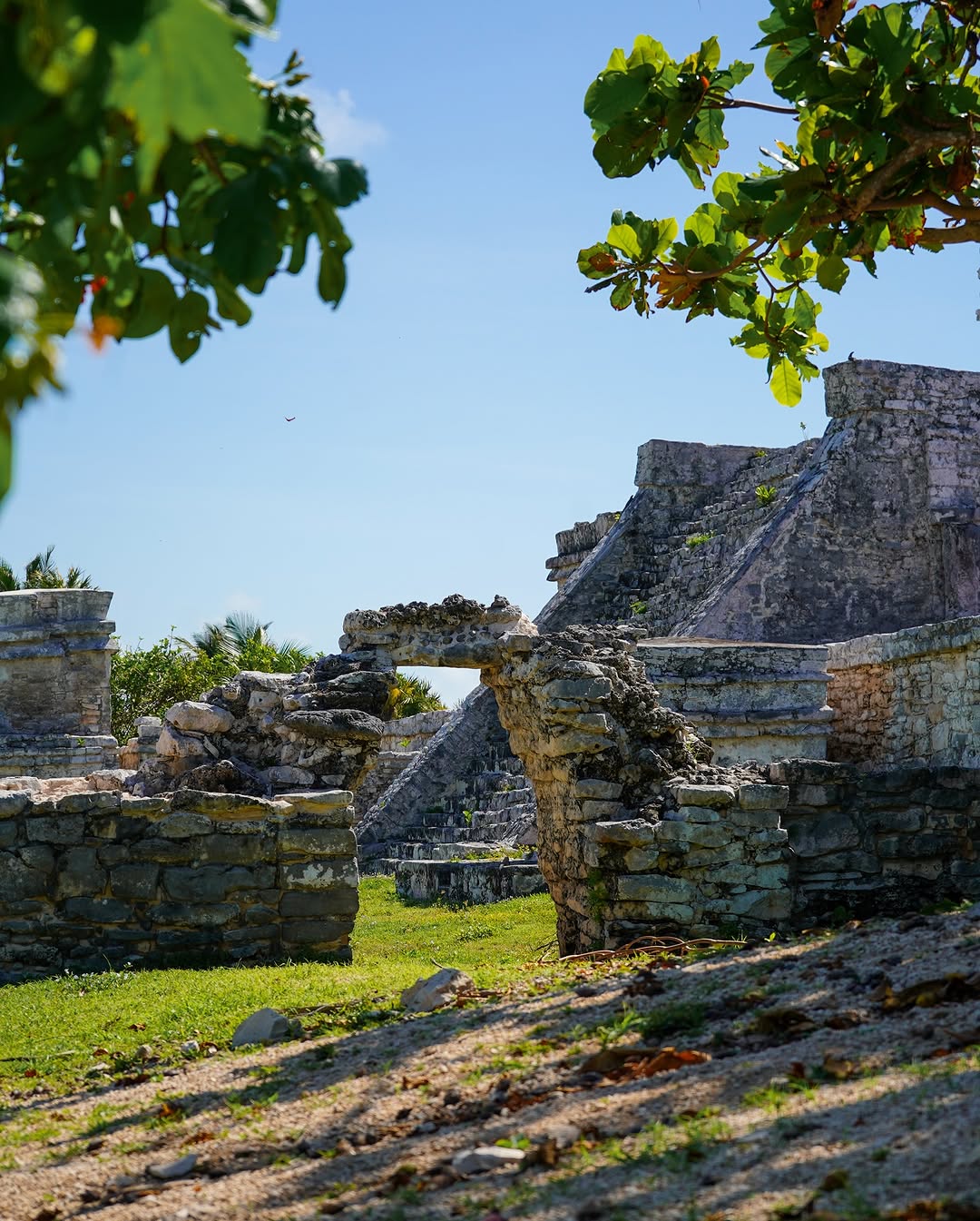 ancient stone ruins with a small arch and pyramid in the background under a clear blue sky