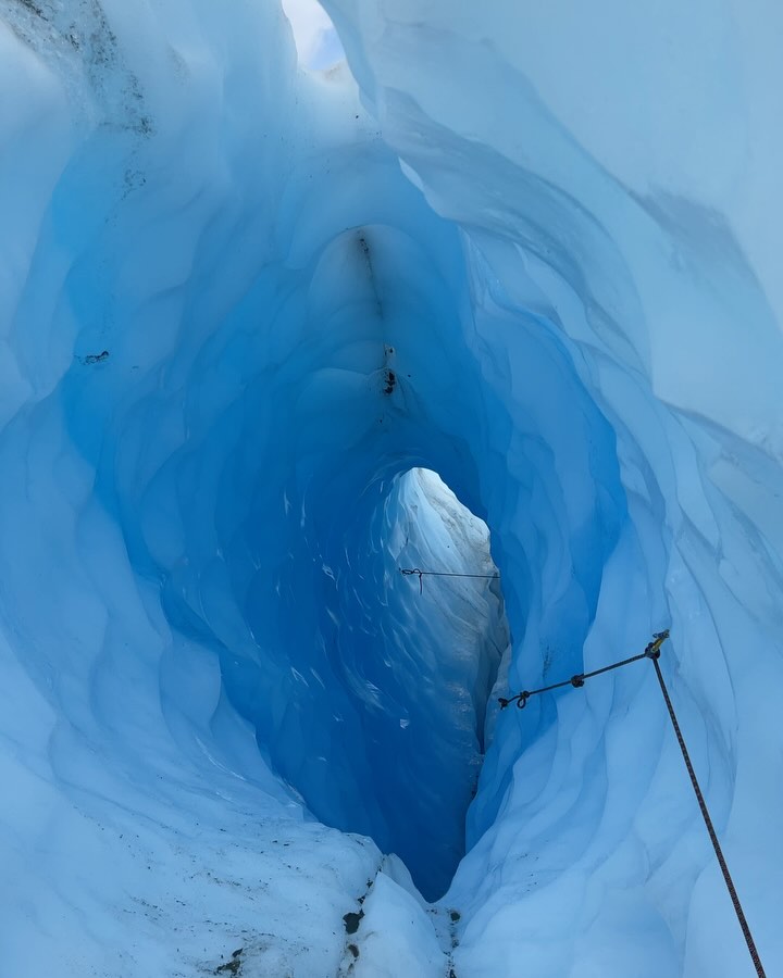 narrow tunnel carved into bright blue ice with ropes for climbing