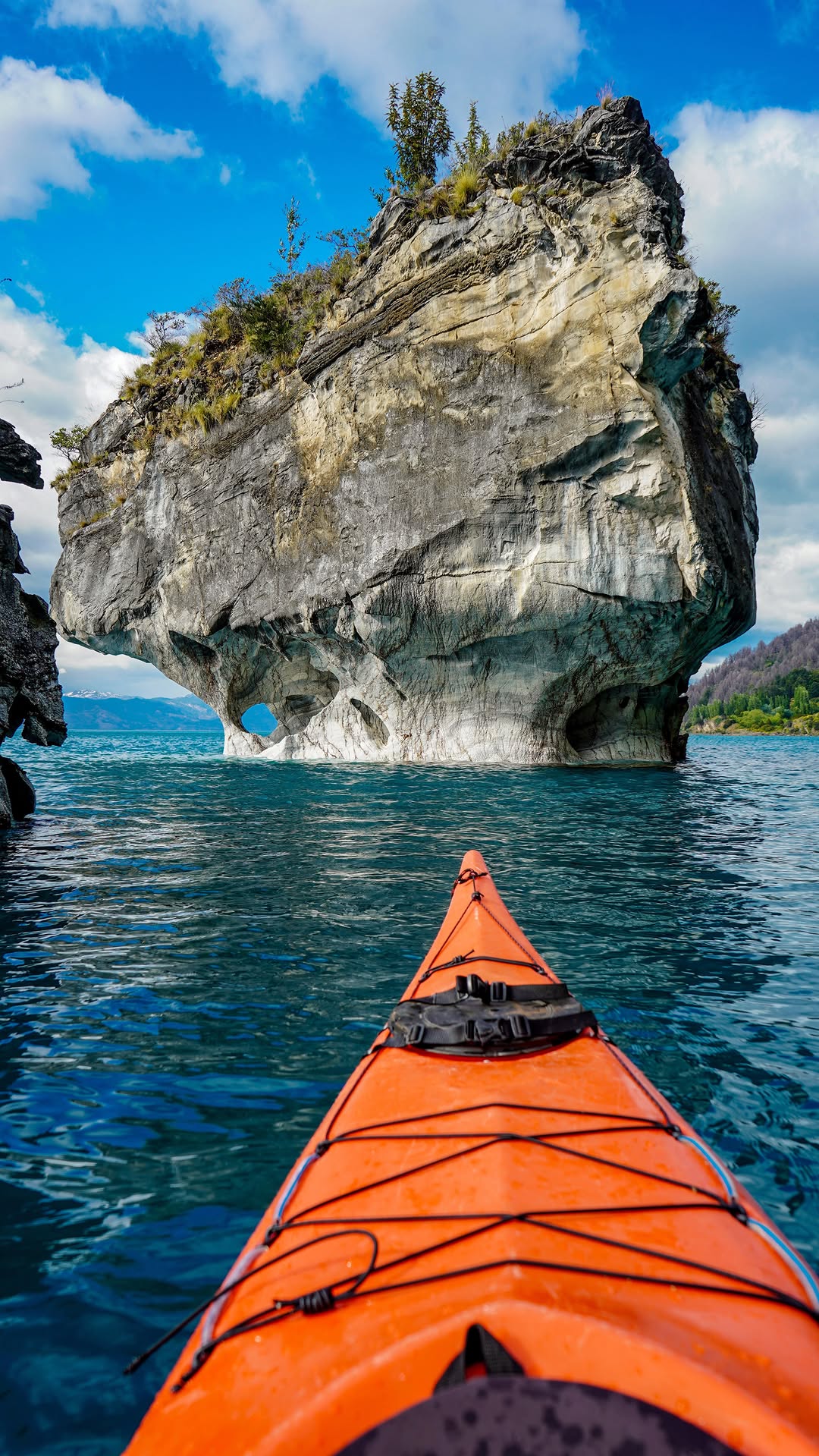 orange kayak approaching a large rock formation in a clear blue lake