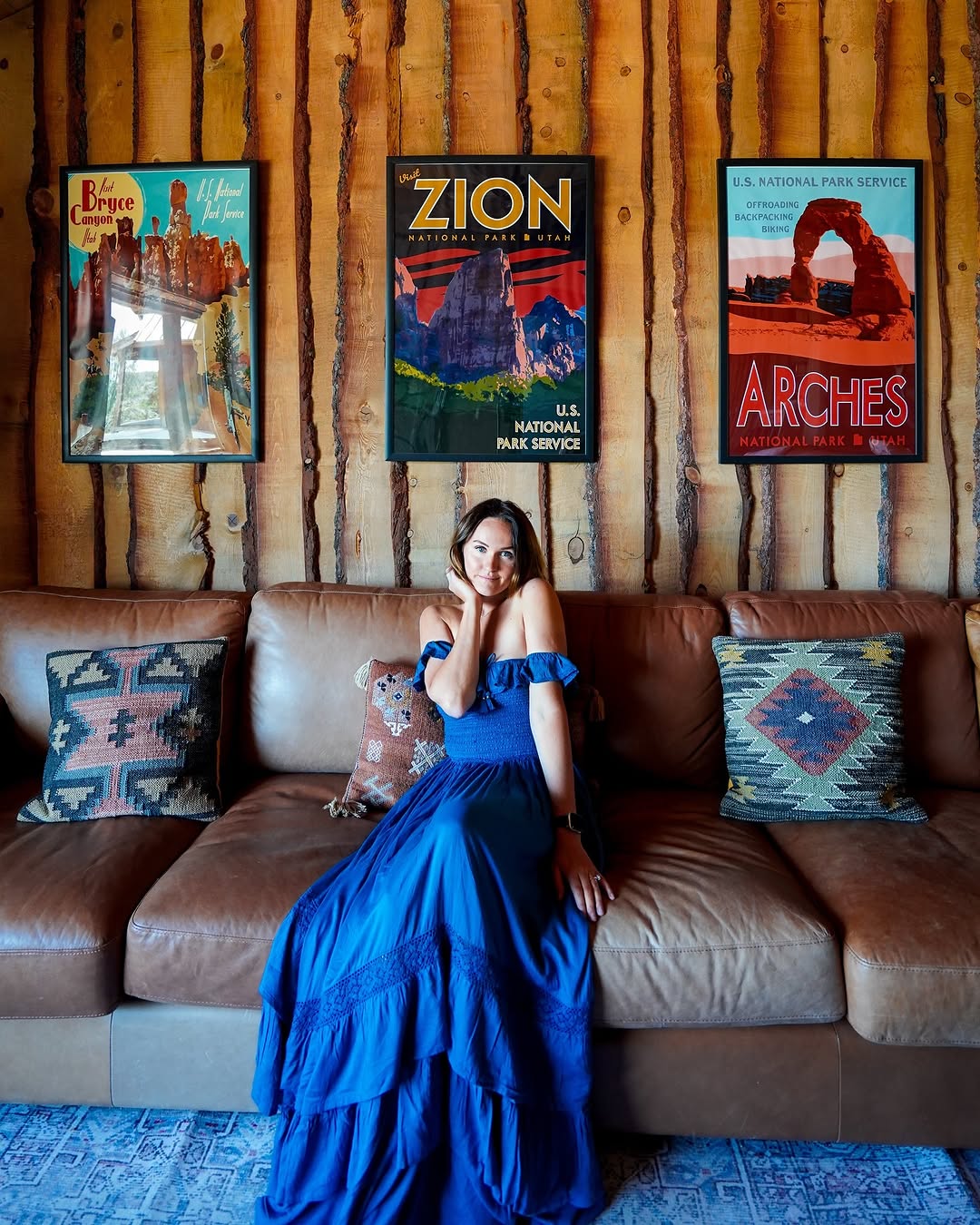 Polina on a leather couch under national park posters inside a cabin at Zion Mountain Ranch