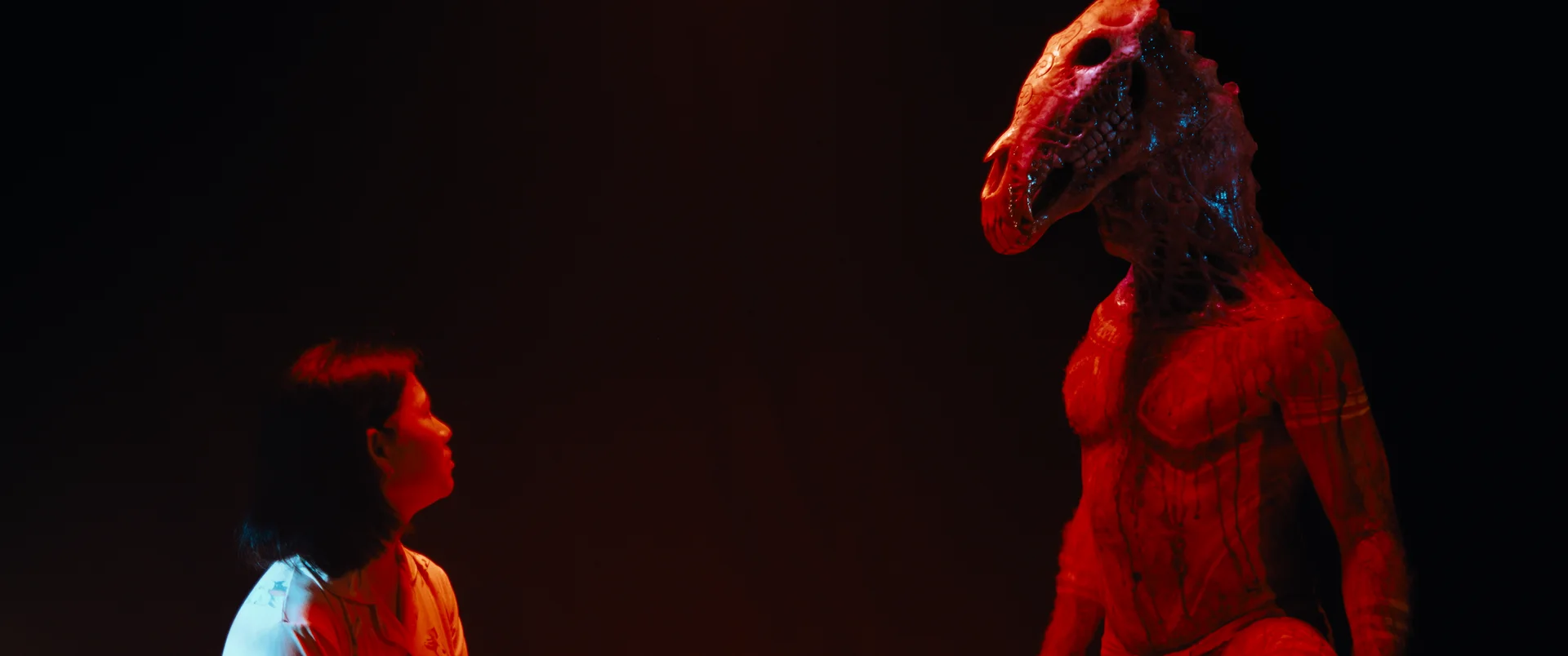 Still from BREEDER: a woman looks up at a red figure with a horse’s head in a dark room