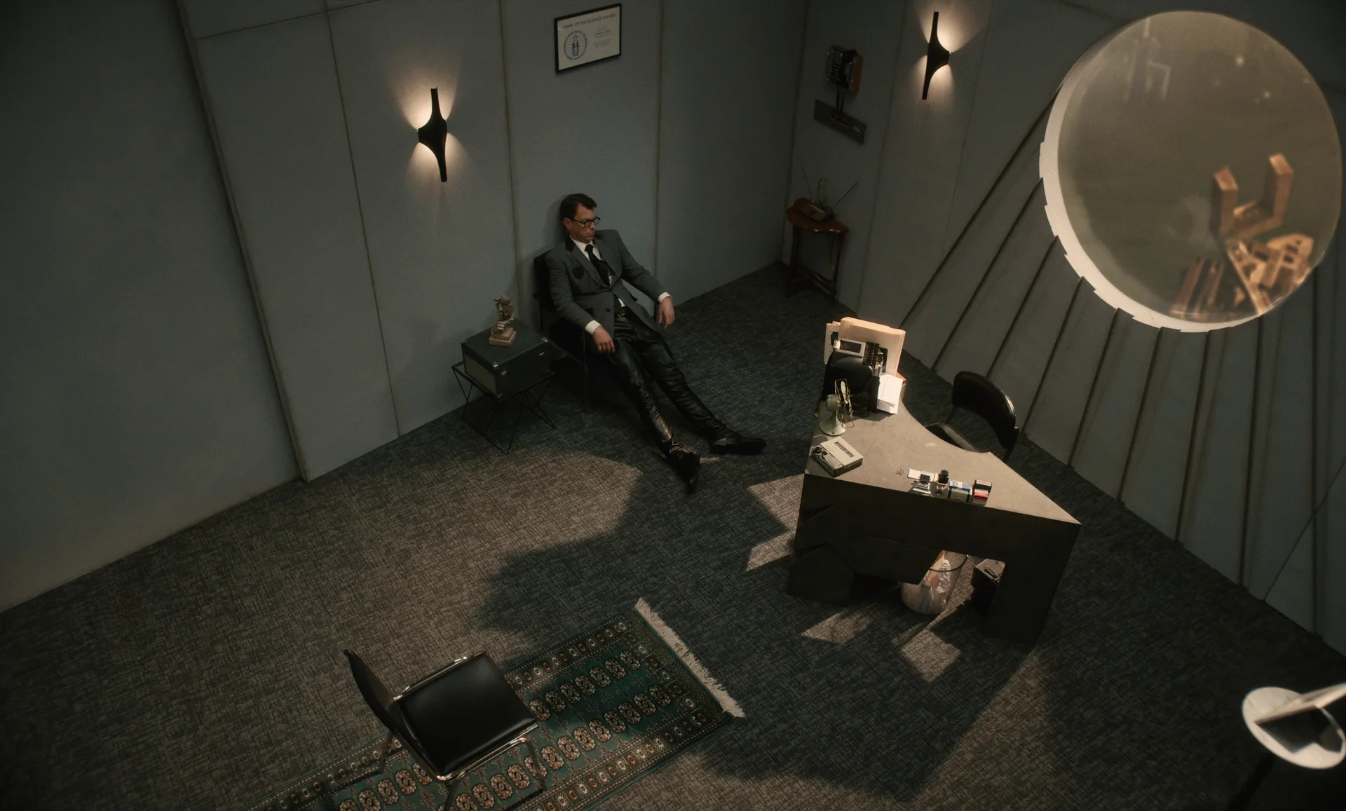 Still from CIVIL SERVICE: an overhead view of a man in a suit slumped in a chair in a gray office