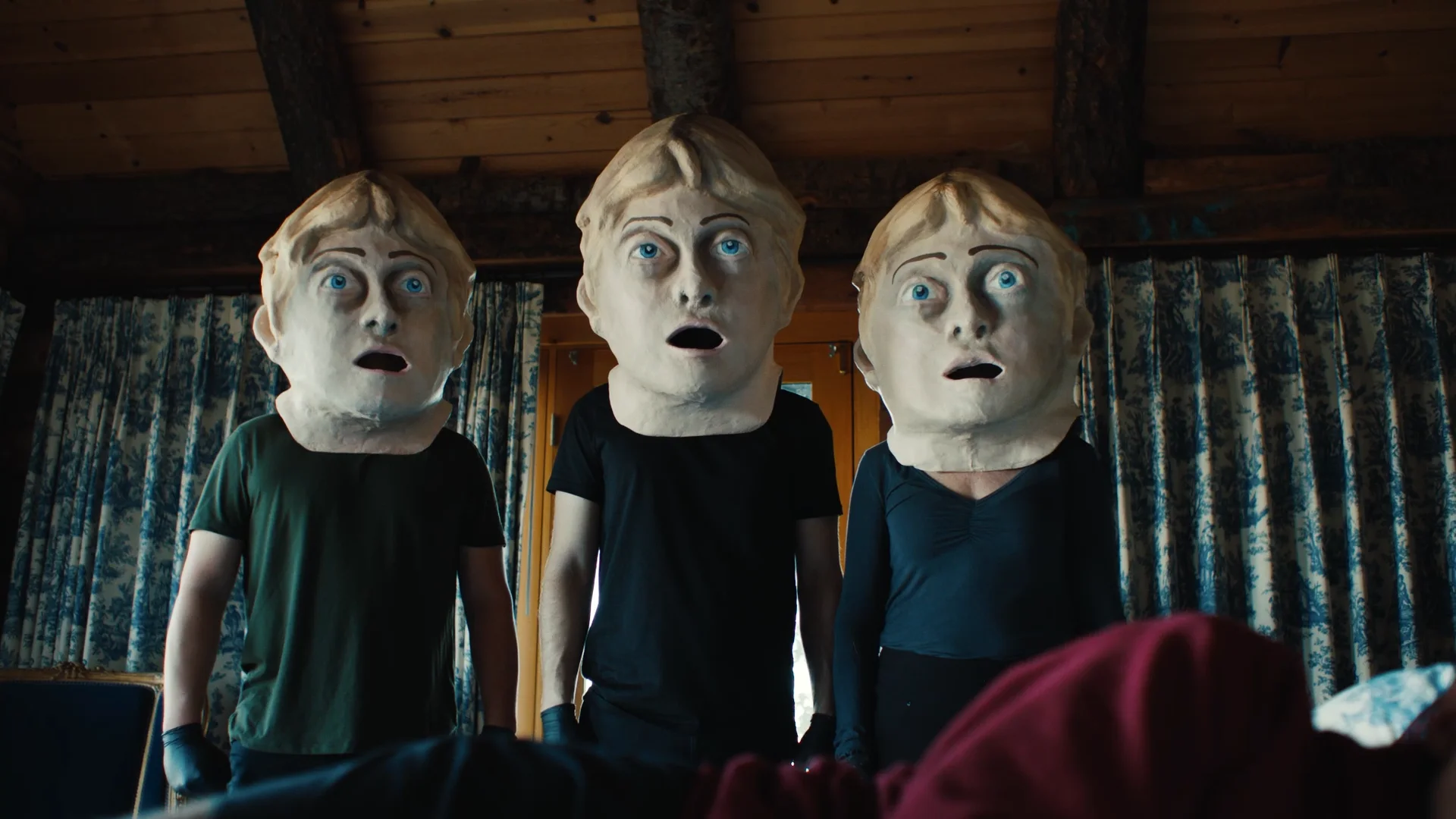 Still from RAT!: three people in identical pale doll-like masks stand side by side in a wood cabin