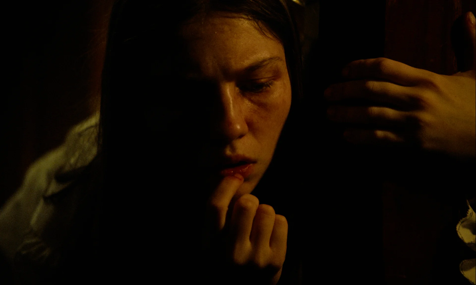 Still from NAIL-BITER: a woman bites her fingernail in a dim room
