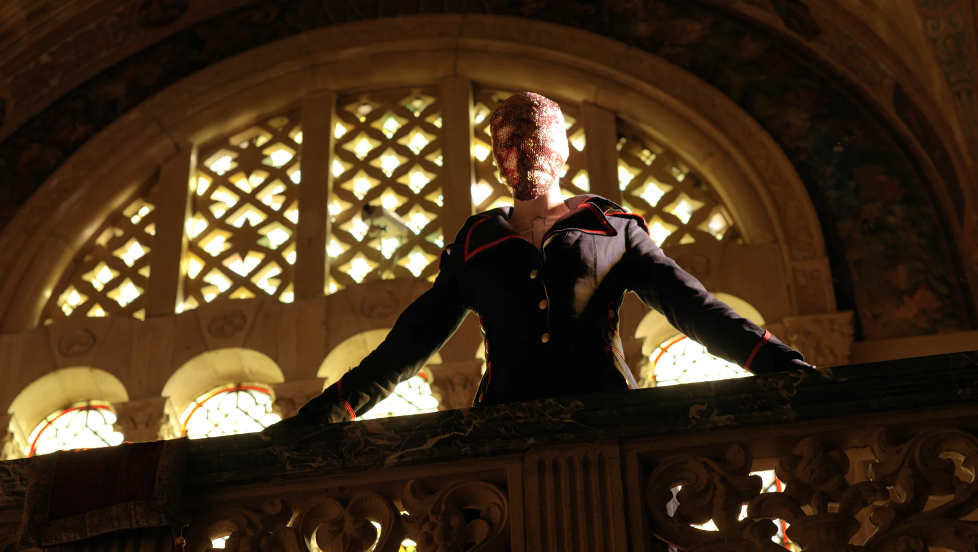 Still from RED RIBBONS IN THE HOUSE OF STAINED GLASS: a masked figure in a dark uniform stands at a stone balcony under a lattice window