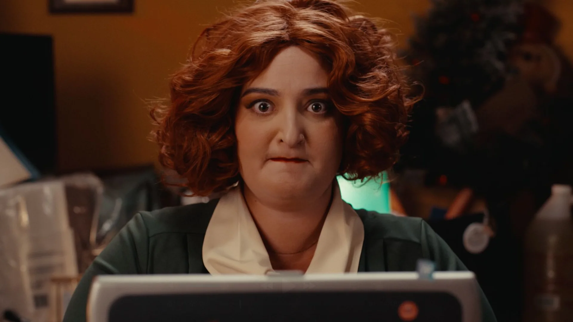 Still from FRANKSLIST: a wide-eyed woman with curly red hair sits behind a computer monitor