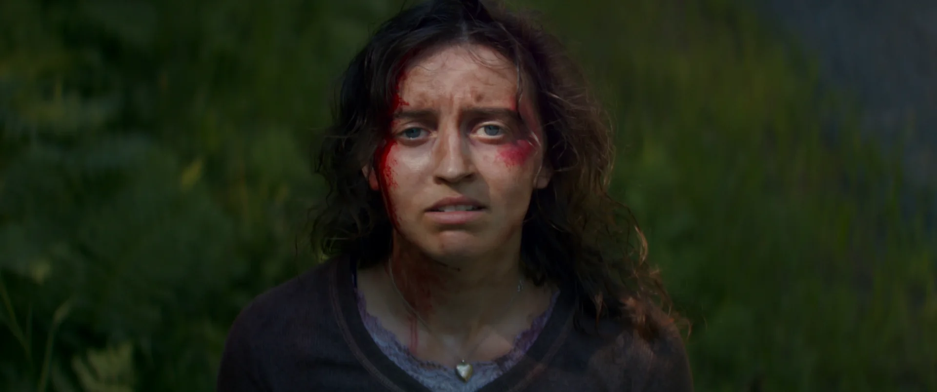 Still from BLOSSOM NEEDS A RIDE HOME: a woman with blood on her face stands in a grassy field