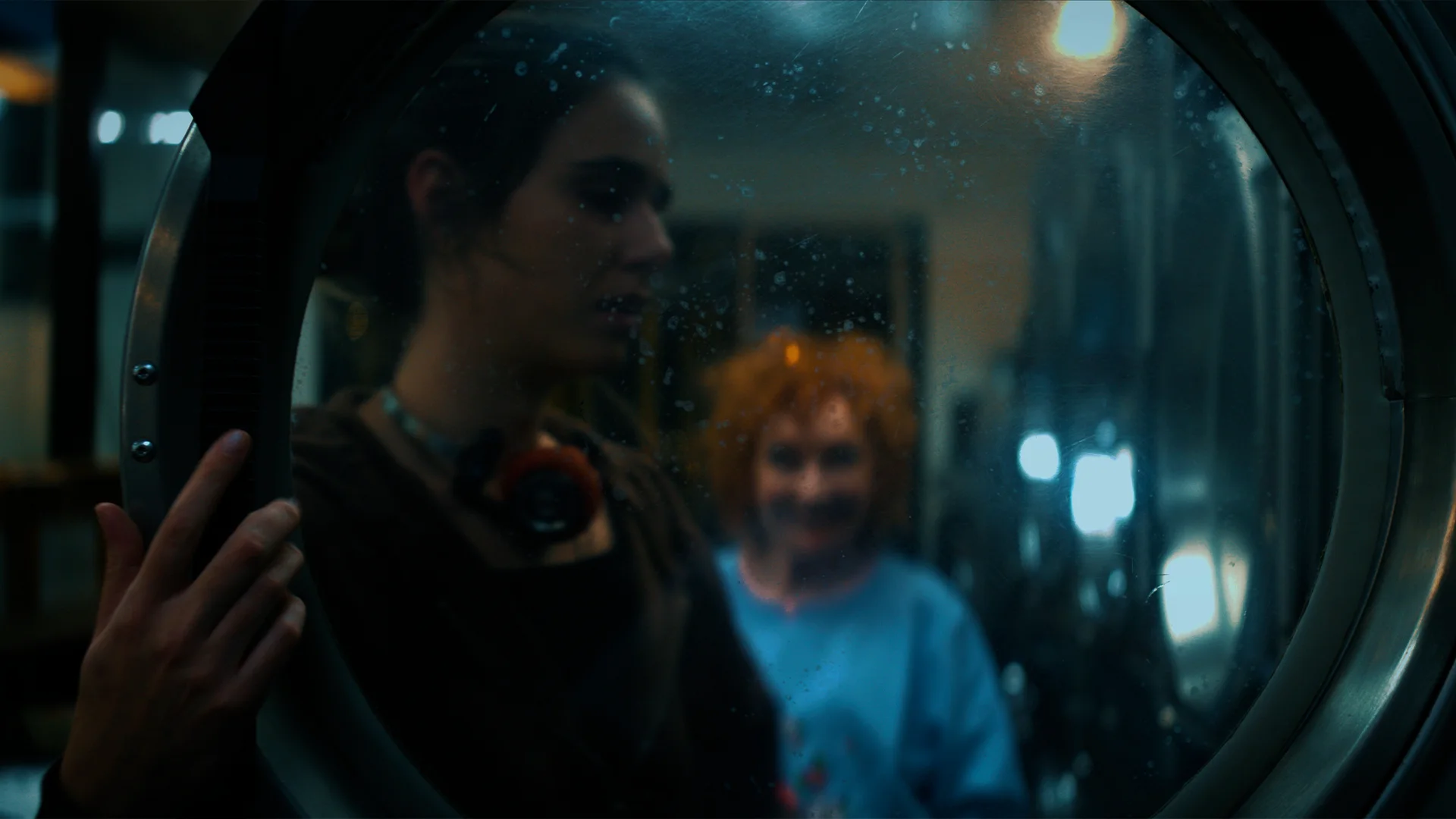 Still from MISSING SOCKS: two women seen through the round glass door of a washing machine