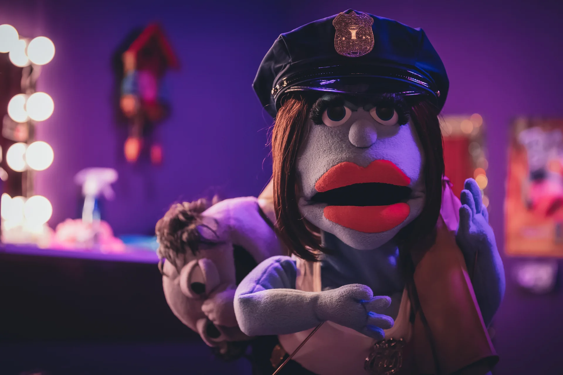 Still from DIRTY FUZZ: a puppet police officer with large red lips stands in a dressing room lit purple